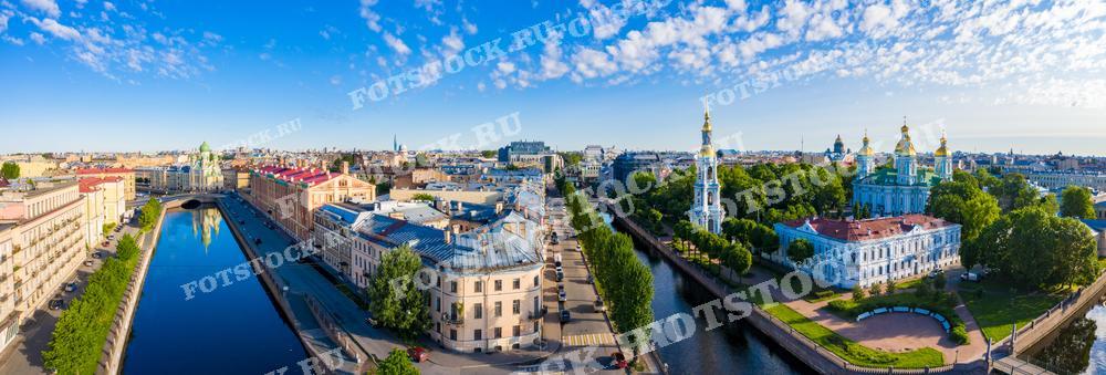 Эта панорамная фотография представляет собой живописный вид на каналы и прилегающую архитектуру Санкт-Петербурга в ясный день. Эта фотография идеально подходит для иллюстрации городских гидов, туристических проспектов, исторических и культурных публикаций, а также может использоваться в качестве рекламного материала для представления культурного наследия и архитектуры города.